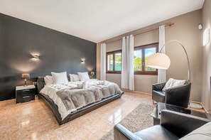 A modern bedroom with a large bed, a nightstand, a chair, and a floor lamp. - Villa Levante Freshly Renovated for 2026 - With Wi-Fi, Air Conditioning, and Heated Pool (Sa Pobla)