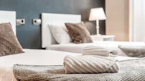 Quarto de hotel com cama, almofadas, abajur e toalha dobrada.