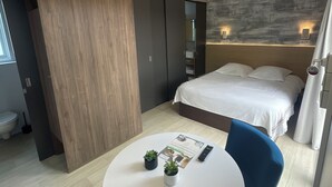 Et moderne hotelværelse med seng, natbord med fjernbetjening, en lille potteplante og en blå stol.