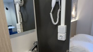 A modern bathroom with a white sink, a hairdryer mounted on the wall, and a bed with white bedding. - Camp'hotel (Mamers)