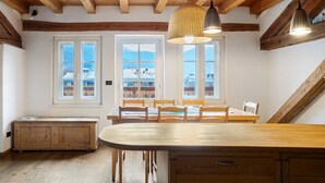 Ein Essbereich mit Holztisch und Stühlen, großen Fenstern mit Ausblick und einer Decke mit freiliegenden Balken.