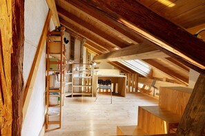 Habitación en el ático con vigas de madera, una escalera y una zona de escritorio.