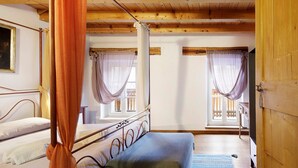 Ein Zimmer mit einem Bett, einem Vorhangfenster, einer Holzbalkendecke und einer Tür.