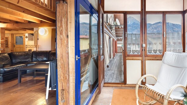 Ein Holzinnenraum mit einem schwarzen Ledersofa, einem weißen Korbstuhl und Bergblick durch große Fenster.