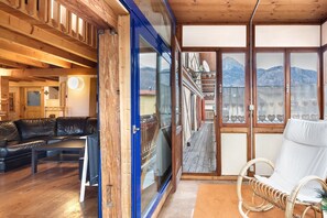 Un interior de madera con un sofá de cuero negro, una silla de mimbre blanco y vistas a montañas a través de amplios ventanales.