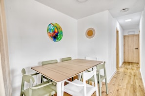 A room with a wooden table and chairs, a colorful wall decoration, and a door leading to another room.
