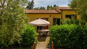 A yellow building with a tiled roof, a patio with a table and chairs, and a covered umbrella.
