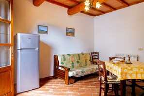A kitchen with a refrigerator, a wooden bench, a dining table with a yellow tablecloth, and two framed pictures on the wall.