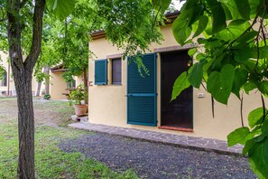 Ein Gebäude mit Ziegeldach, einer Tür mit Fenster und einem kleinen Gartenbereich mit Baum und Topfpflanze.