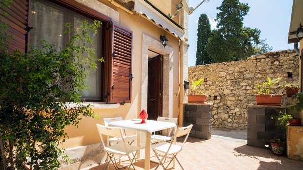 Patio esterno con tavolo e sedie, piante in vaso e un muro in pietra.