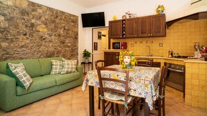 Un soggiorno accogliente con un divano verde, un tavolo da pranzo con sedie, angolo cottura con mobili in legno e una televisione a schermo piatto montata a parete.