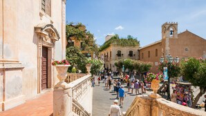 Una via storica con edifici in pietra, una torre campanaria e un marciapiede.