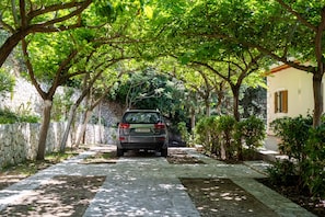 A paved pathway leading to a building with a stone wall on one side and a tree-lined street on the other.