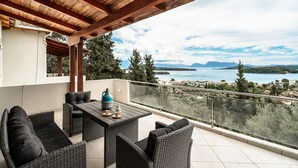 Un balcón con mobiliario de mimbre, una mesa y vistas a un lago y montañas.