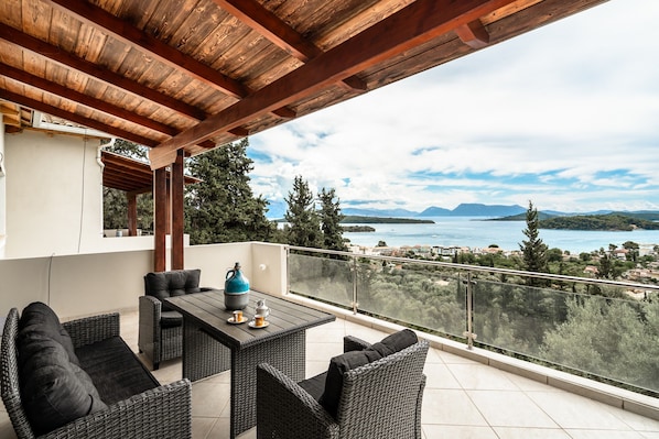 A balcony with wicker furniture, a table, and a view of a lake and mountains.