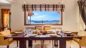 Un comedor con una mesa preparada para cuatro personas, vista al mar y una ventana con un dosel a rayas.