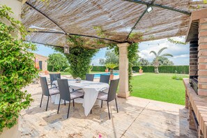 Une terrasse extérieure avec une table et des chaises, une pergola et une vue sur une piscine et un jardin.