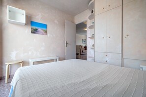 Un dormitorio con cama, una mesita, un armario y un cuadro en la pared.