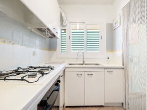 Una cocina compacta con estufa a gas, pileta y muebles blancos.