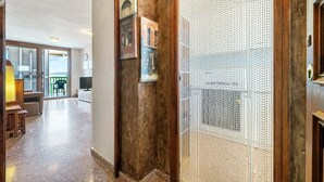 A hallway with a wooden door, a textured wall, and a view of a living area with a TV and furniture. - 'Mirador Altafulla' 5th Floor with Two Terraces and Elevator (altafulla)