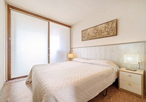 Une chambre à coucher avec un lit, une table de chevet, une lampe, une porte coulissante et un tableau au mur.