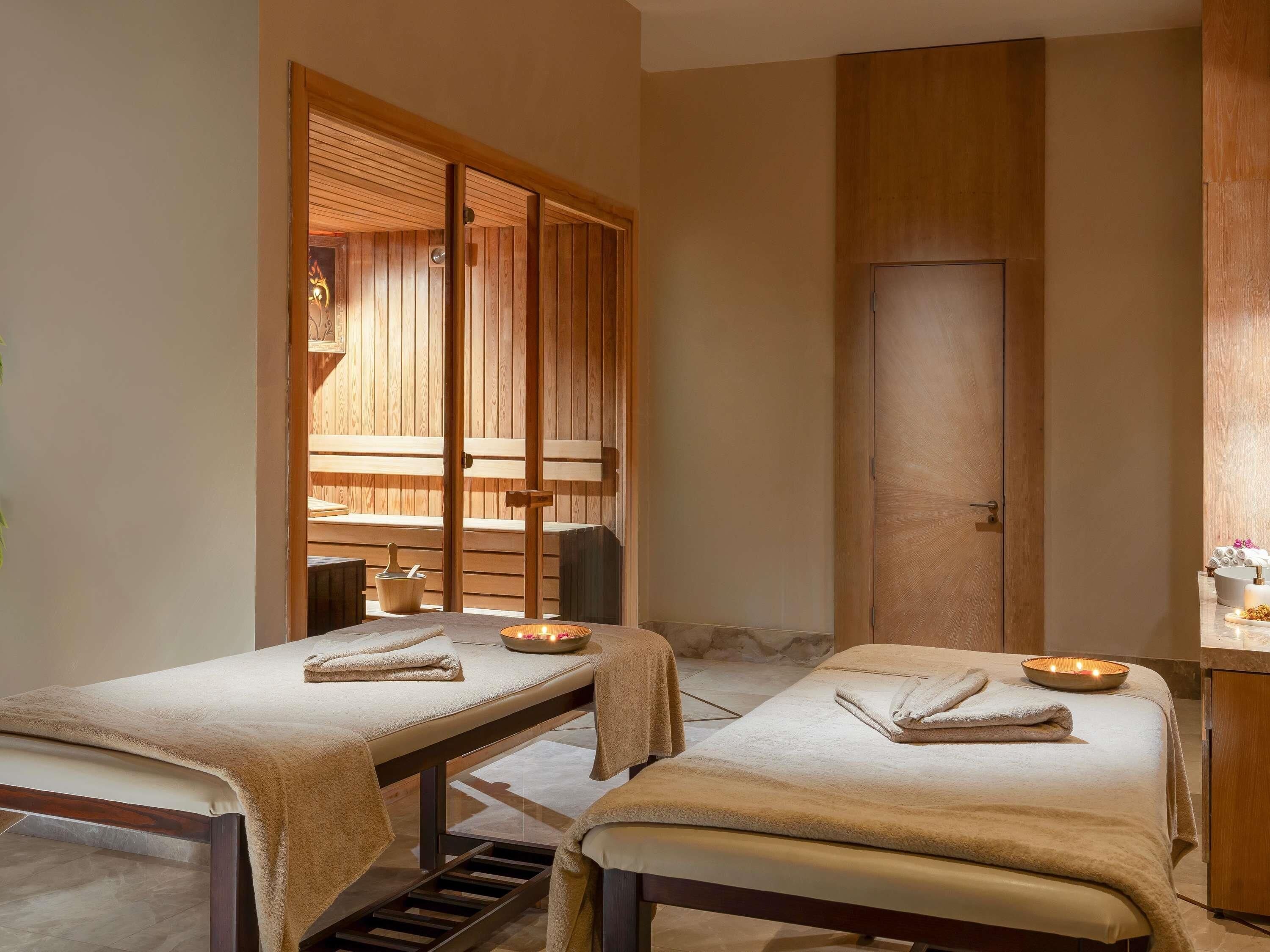 Un cuarto de spa con dos camillas de tratamiento, una puerta corredera de madera y una pequeña zona de estar.