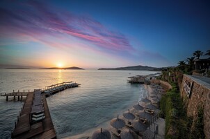 Un complejo turístico frente al mar con un muelle de madera que se adentra en el océano, sombrillas de playa y un muro de piedra con un letrero.
