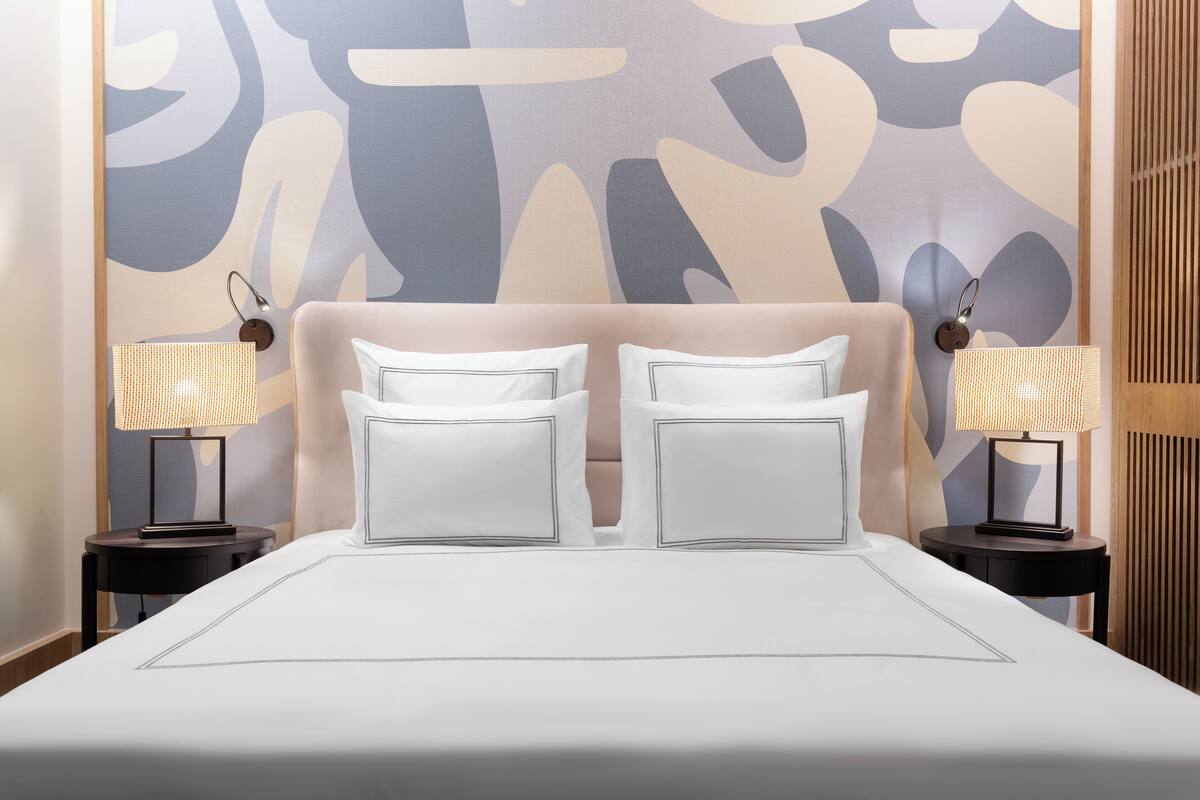 A neatly made bed with white linens, two bedside tables with lamps, and a large abstract-patterned wall behind the bed.
