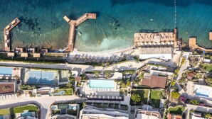 An aerial view of a resort with a clear blue sea, a swimming pool, and multiple buildings with a modern architectural style. - Swissôtel Living Bodrum (Bodrum)