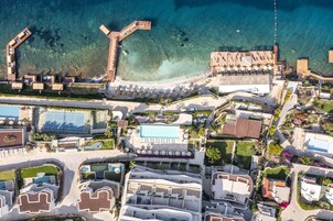 Vista aérea de un resort con mar azul turquesa, piscina y varios edificios de estilo arquitectónico moderno.