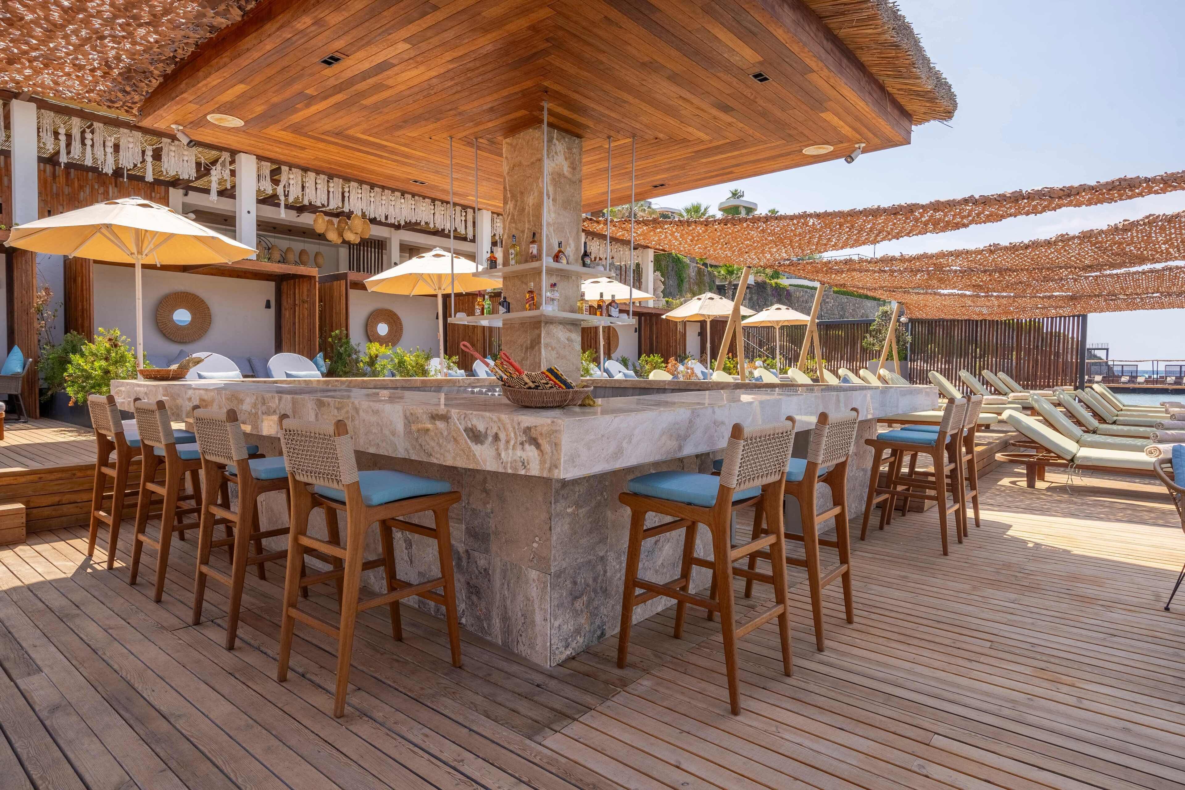 A wooden deck with a bar area, lounge chairs, and umbrellas.