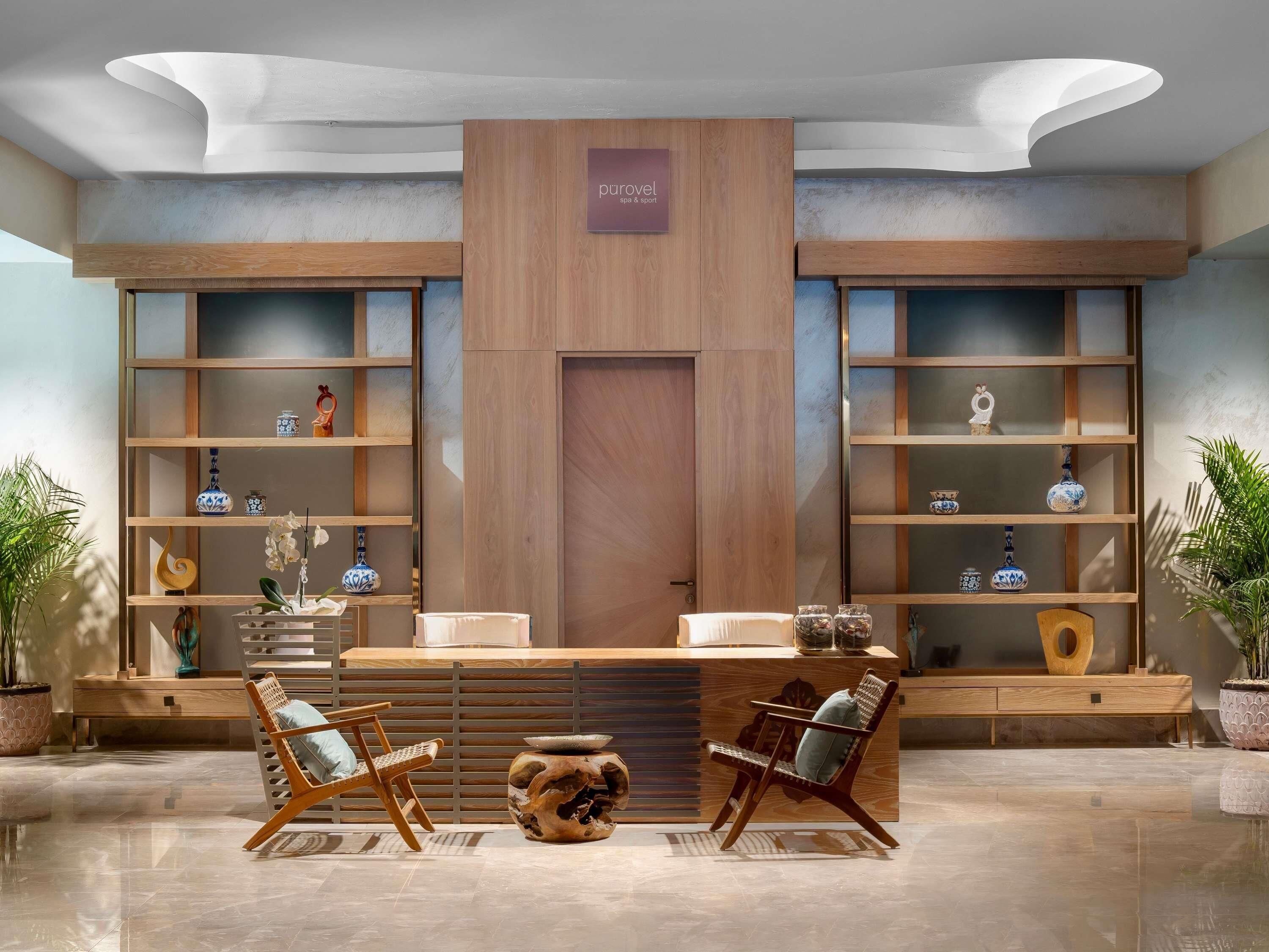 Un área de recepción con un mostrador de madera, dos sillas y estanterías con objetos decorativos.