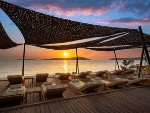 Une terrasse en bois avec des chaises longues et une vue sur le coucher de soleil sur l’eau.