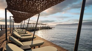 A wooden deck with lounge chairs and a canopy, overlooking calm water and distant land. - Swissôtel Living Bodrum (Bodrum)