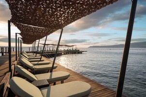 A wooden deck with lounge chairs and a canopy, overlooking calm water and distant land.