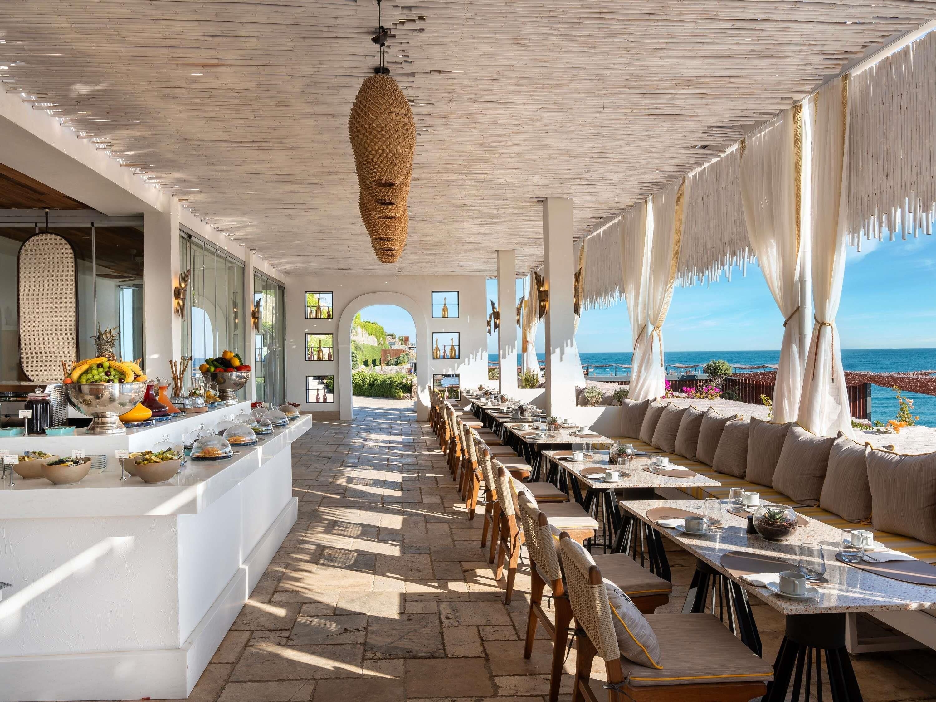 Un ristorante sul mare con posti a sedere all'aperto, un buffet con frutta e bevande e vista sull'oceano.