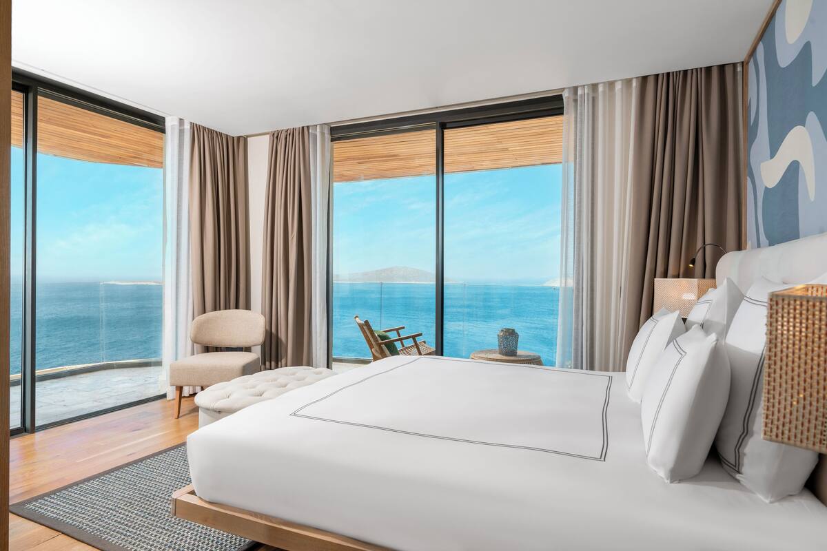 A modern hotel room with a large bed, a view of the ocean, and a balcony with a chair.
