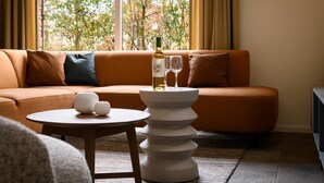Un salon moderne avec un canapé, une table ronde surmontée d’un vase blanc et une bouteille de vin posée sur un présentoir blanc à plusieurs niveaux.
