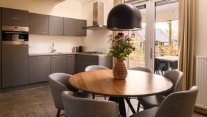 Une cuisine moderne avec des meubles gris, un four encastré et un coin repas comprenant une table ronde en bois et des chaises grises.