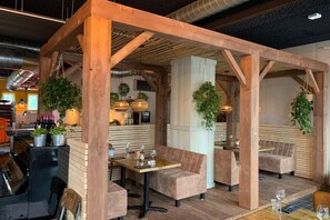 Een gezellig restaurant met houten balken, zachte zittingen en hangplanten.