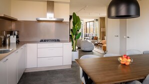 A modern kitchen with a central island, a dining area with a wooden table, and a large black pendant light.