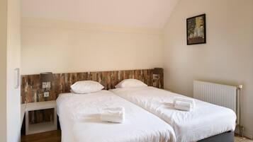 Une chambre double avec deux lits, une tête de lit en bois, une table de chevet, une lampe et un tableau encadré au mur.