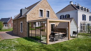 A modern house with a glass-enclosed patio, stone facade, and a well-maintained lawn.