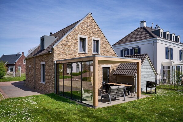 Een modern huis met een glazen terras, een gevel van natuursteen en een verzorgd gazon.
