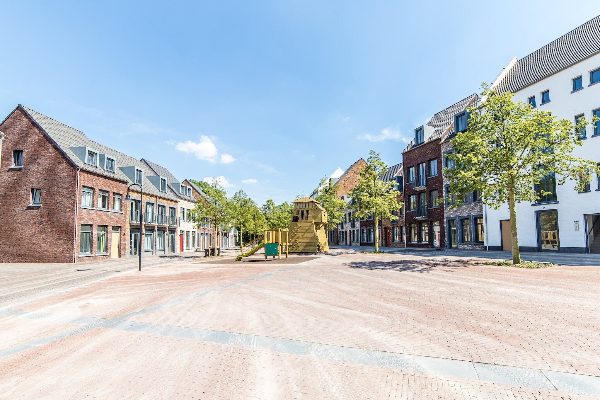 Ruim voetgangersgebied met een speeltuin, omgeven door moderne gebouwen met bakstenen gevels en grote ramen.