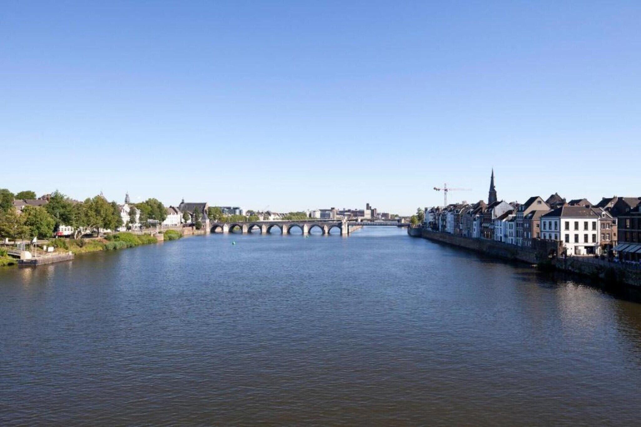 En flod med en stenbro, byggnader längs flodstranden och en klar himmel.