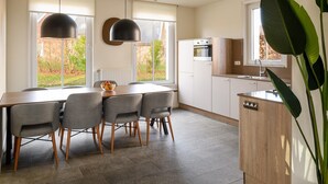 A modern kitchen with a dining table and chairs, a built-in oven, and a large window with a view of the outdoors.