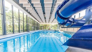 An indoor swimming pool with clear blue water, large windows, and a blue water slide.