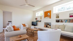 Una sala de estar con sofá, sillón, mesa de centro, televisor y estanterías con adornos.