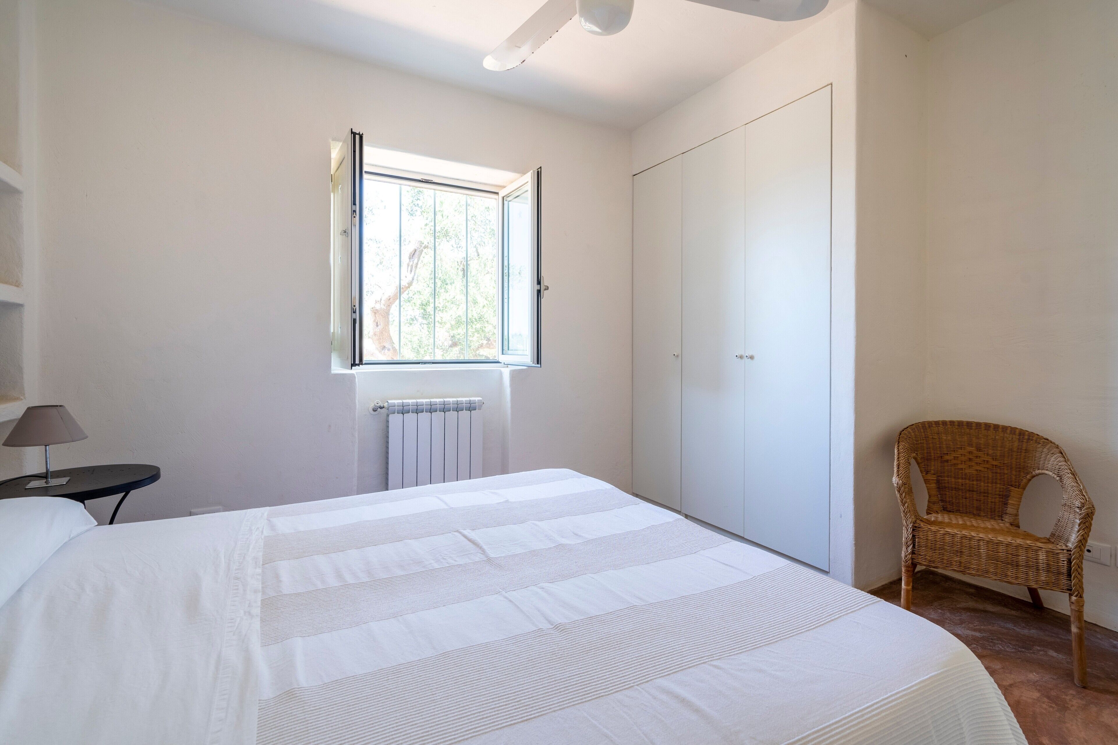 Un dormitorio con cama, ventana, radiador, silla y armario.